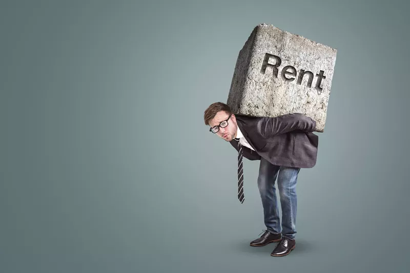 Image: well-dressed hunched man with what looks to be a very heavy concrete block on his back with the word "Rent" etched into it (Conceptual image of a man burdened by high rent)