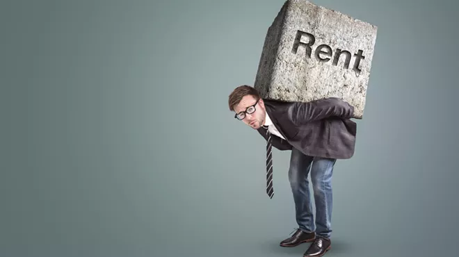well-dressed hunched man with what looks to be a very heavy concrete block on his back with the word "Rent" etched into it (Conceptual image of a man burdened by high rent)
