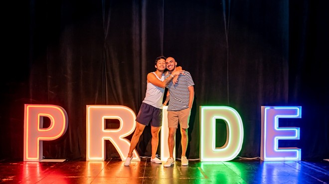 A gay couple in front of letters that spell out Pride
