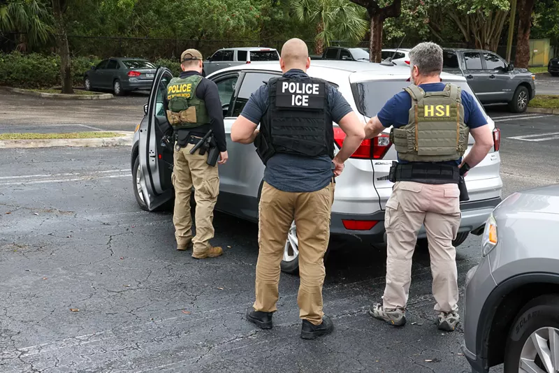 Image: Immigration enforcement officers stand outside a parked vehicle,