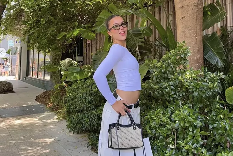 Image: a young girl poses with a purse in front of greenery