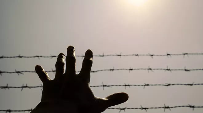 A hand reaching before a barbed wire fence