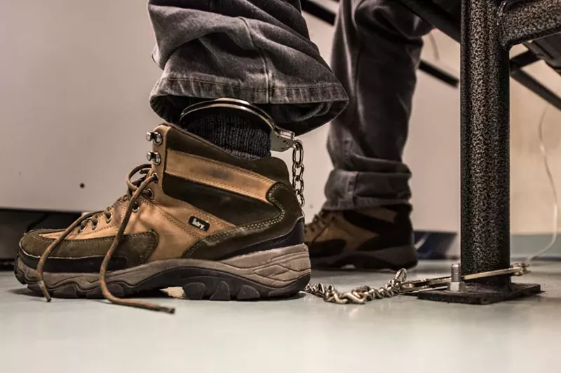 Image: A photo of a detainee handcuffed to a bench.