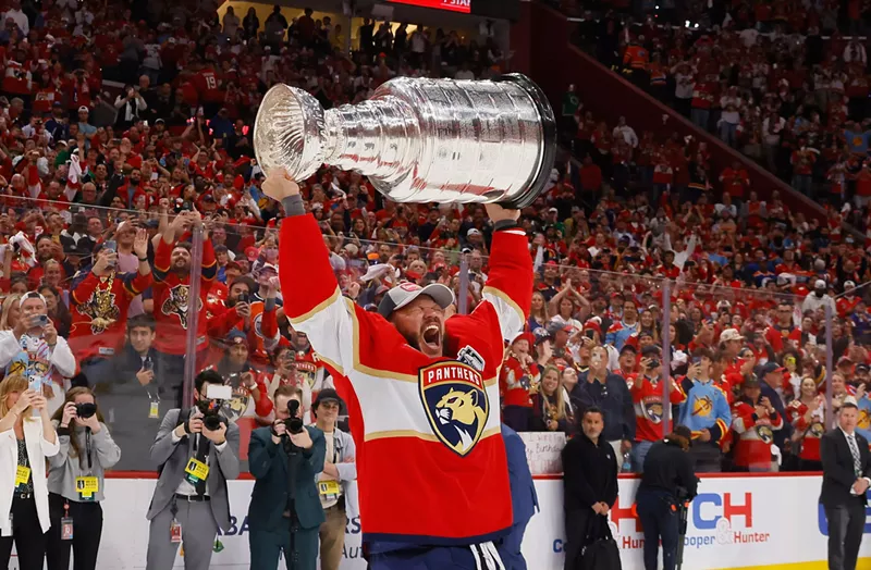 Image: Panthers player Kyle Okposo lifts the Stanley Cup over his head on the ice in his home arena and yells out triumphantly