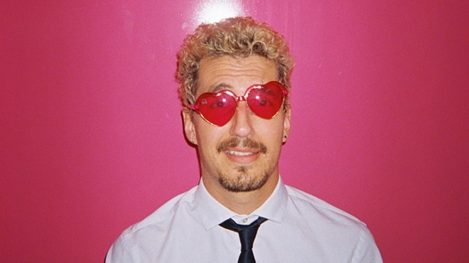 Josch wears heart-shaped sunglasses standing against a bright pink background
