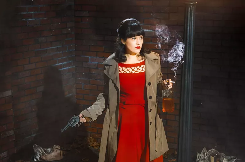 Image: Improv performer in a red dress holding a gun, bottle of whiskey, and cigarette