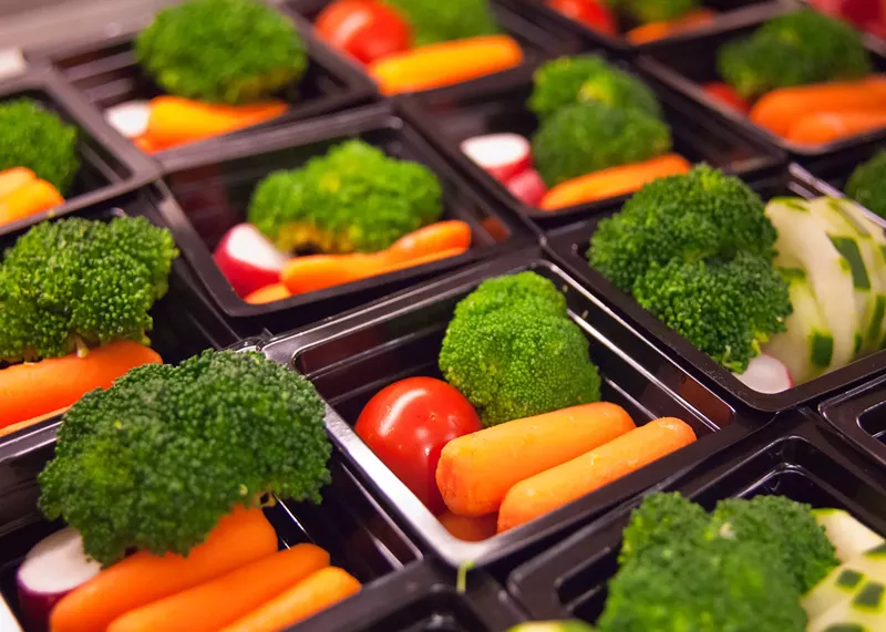 Image: Portions of vegetables like carrots, tomatoes, and broccoli in small black trays