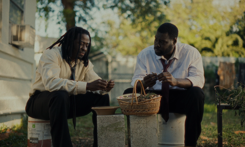 Image: two men sit on buckets in a yard making a basket