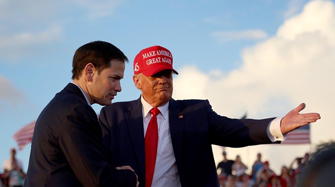 Donald Trump in a "Make America Great Again" cap shakes Marco Rubio's hand in front of a large crowd while directing him to the podium at a Miami-Dade rally