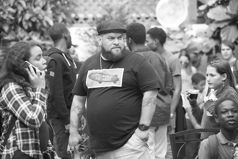 Image: Black and white picture of a man with tattoos wearing a hat.
