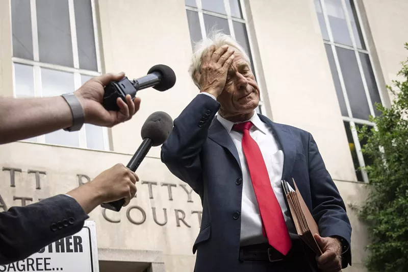 Image: A Donald Trump adviser places a hand on his forehead as reporters stick out their microphones in front of a federal court