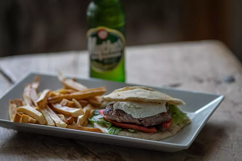 Image: A Greek burger is made with a beef/chicken patty with tzatziki and served with Greek fries.