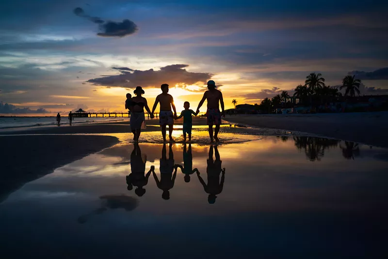 Image: A silhouette of a family walking on a beach at sunset