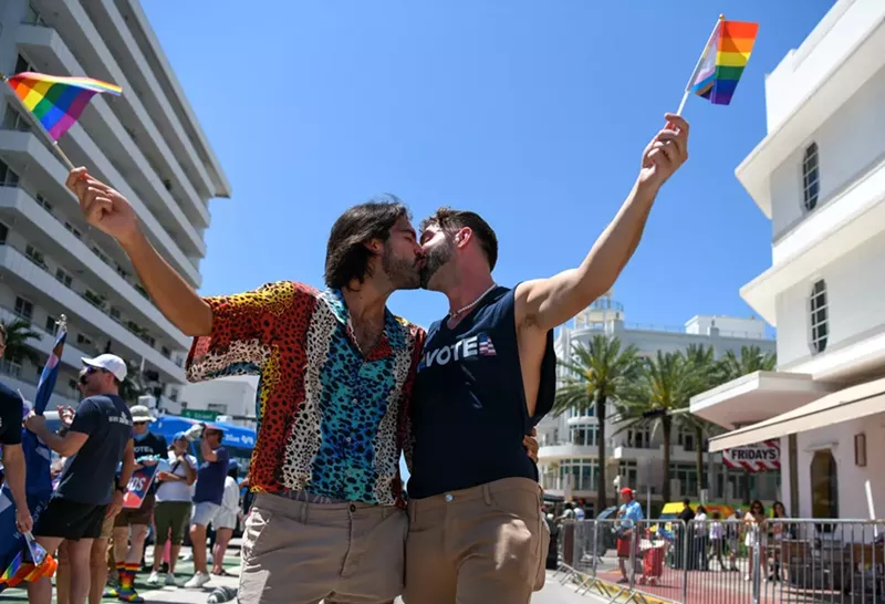 Image: Two men kissing while holding gay pride flags
