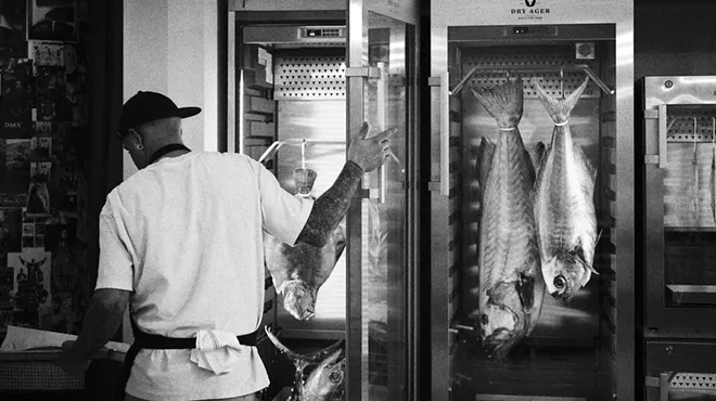 A man looks at fish in a fridge wearing a white shirt