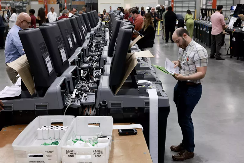 Image: County workers hovering around rows of voting machines