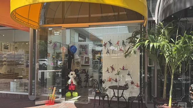 Miami Art Gallery Gift Shop glass storefront, which has a Mickey Mouse sculpture at its entrance, along with a yellow awning.