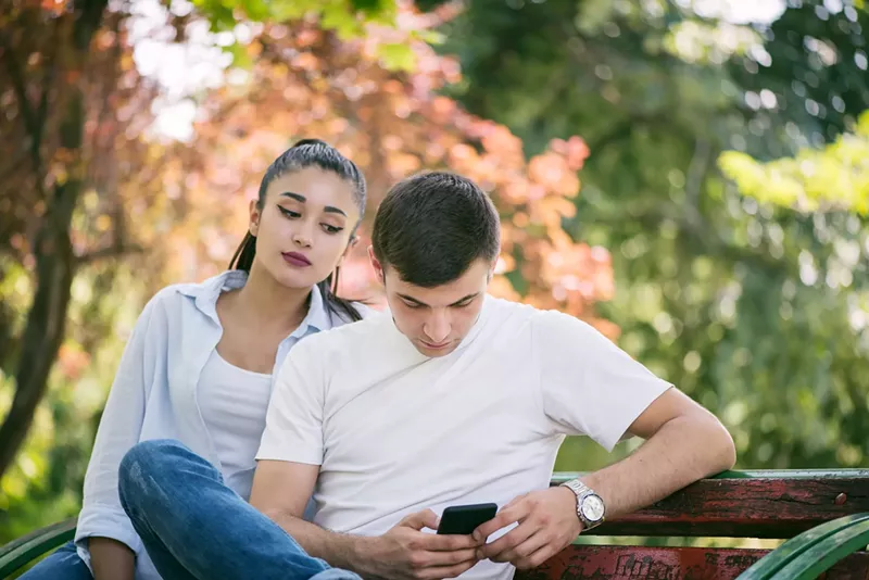 Image: A woman looking over a man's shoulder at his phone