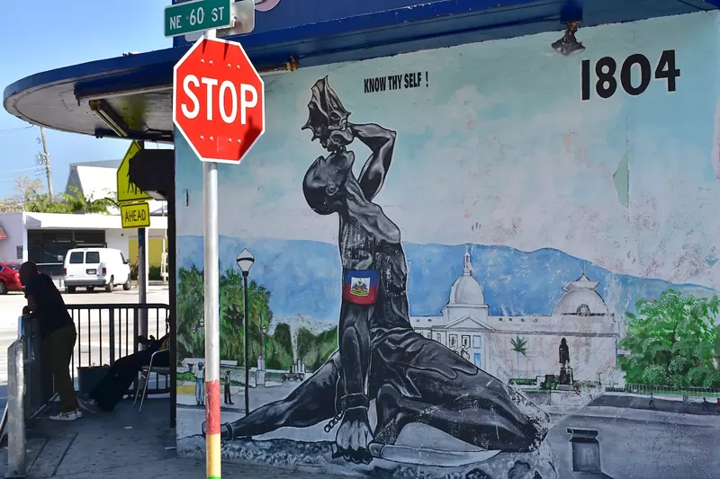 Image: "Know Thy Self": A mural depicting a dark-skinned man with broken shackles holding a machete in one hand and blowing a conch "Freedom Horn" he holds in the other