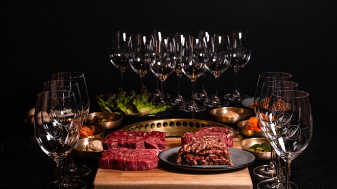 Raw steaks on a cutting board surrounded by empty wine glasses