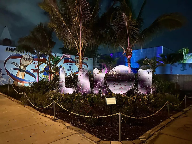 Image: Picture of a sign in between palm trees at night