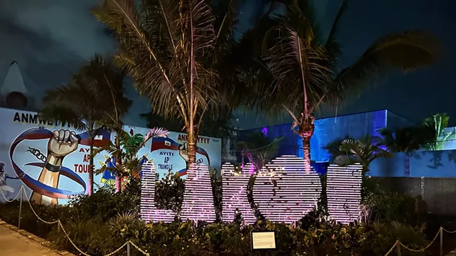 Picture of a sign in between palm trees at night