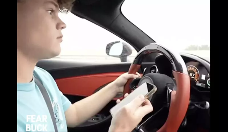 Image: Jack Doherty sitting behind the wheel of his McLaren and holding his cellphone in his right hand