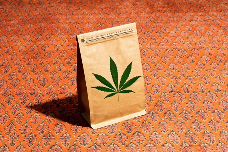 Image: A brown paper bag with a marijuana symbol on it against an orange background