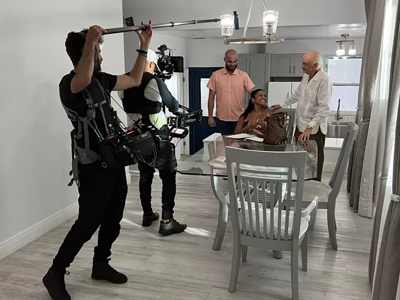 Image: a camera operator and man with a boom mic record an acting scene with two men and a woman at a dining room table