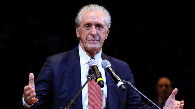 Pat Riley stands in a suit in front of a podium