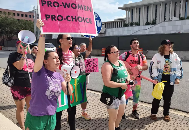 Image: photo of a group outside the Florida Supreme Court, holding megaphones and pink signs with slogans such as "Pro-Women Pro-Choice"