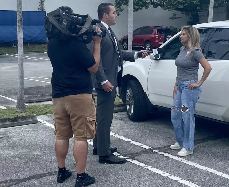 Image: television reporter and cameraman interview a woman standing next to her white car