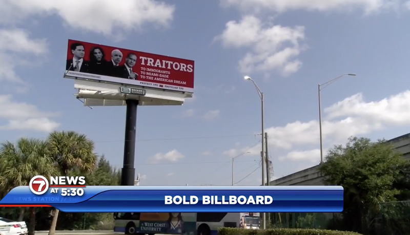 Image: A photo of a red billboard with four politicians on it and the words: “TRAITORS: To Immigrants, To Miami-Dade, To The American Dream” above a blue sky