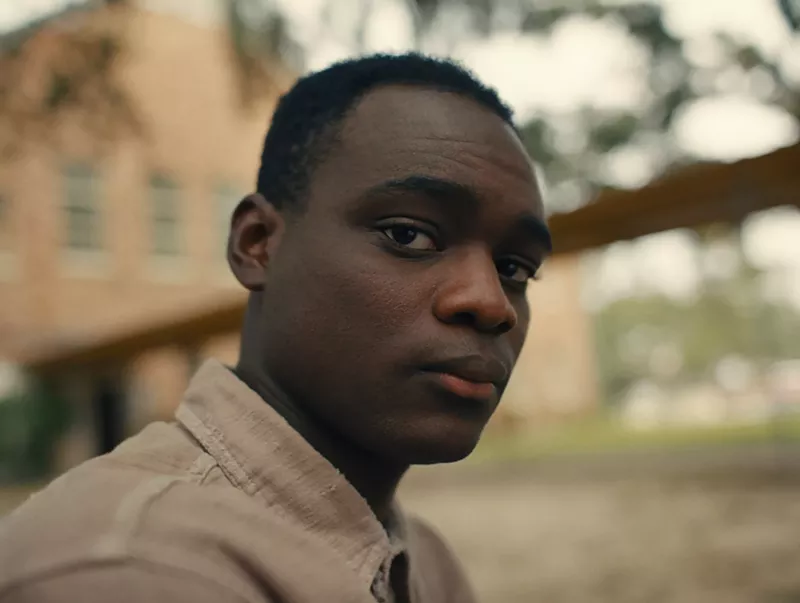 Image: Still of the film Nickel Boys, with a close-up of Elwood (Ethan Herisse) staring into the camera.