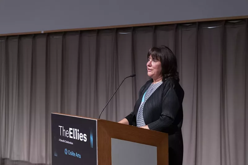 Image: Maria Elena Angulo behind a podium, speaking at the Ellies Awards