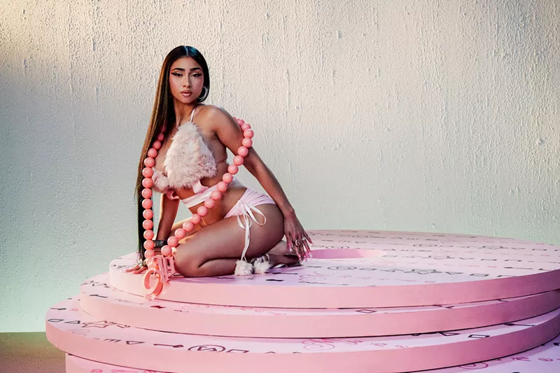 Image: A woman is posing, sitting on a pink rug.
