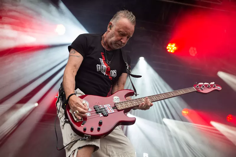 Image: Peter Hook plays bass onstage with stage lights behind him