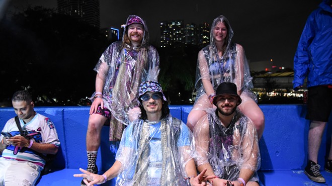 Four people in ponchos seated on blue plastic seats