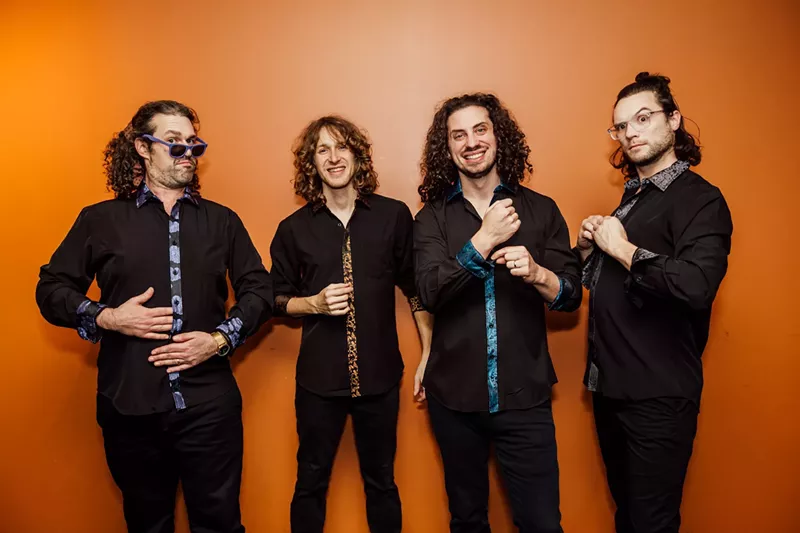 Image: The four members of Pigeons Playing Ping Pong against a bright orange wall
