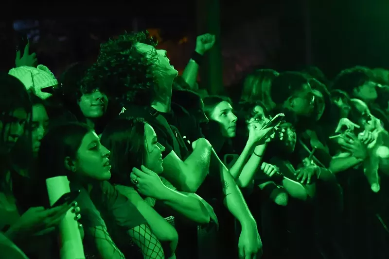 Image: Fans at the front row of a 100 gecs concert bathed in green light