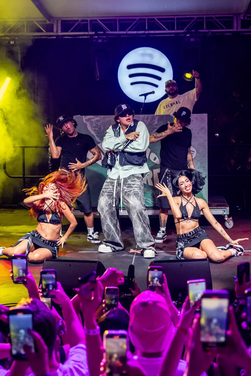 Image: A man performing on stage with dancers and a Spotify logo in the back.