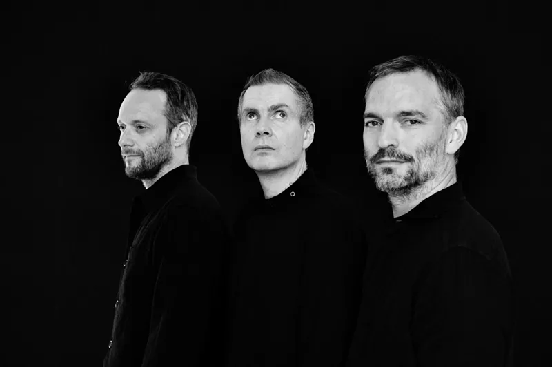Image: a black and white photo of the three band member's faces