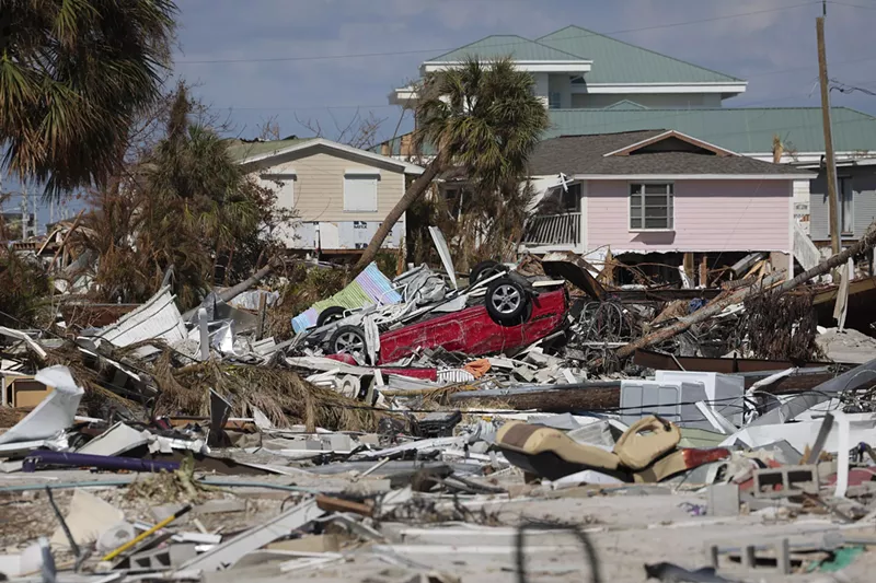Image: Building remnants, giant piles of debris, and an overturned car in the wake of Hurricane Ian