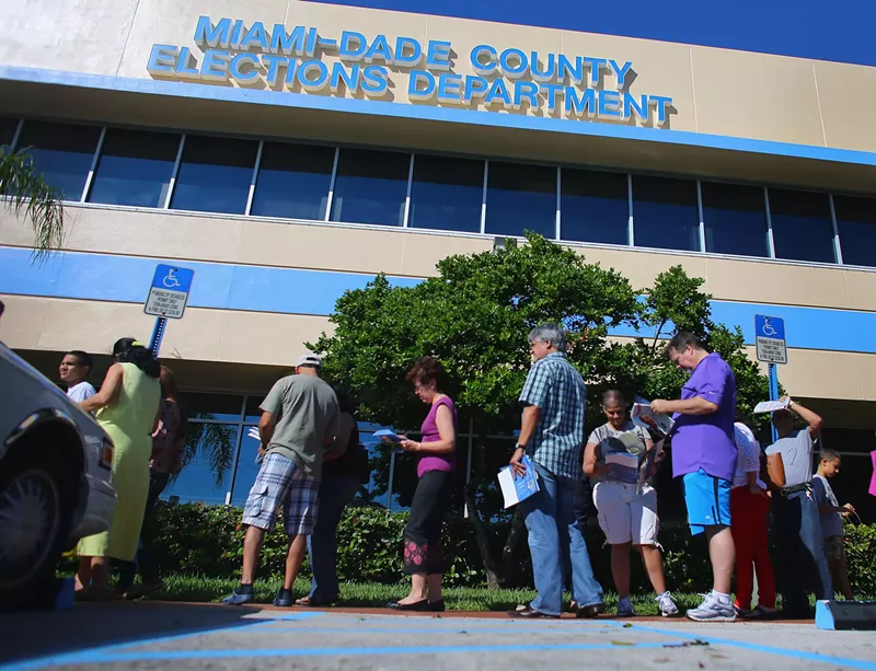 Image: A small group of residents stand outside a county elections building