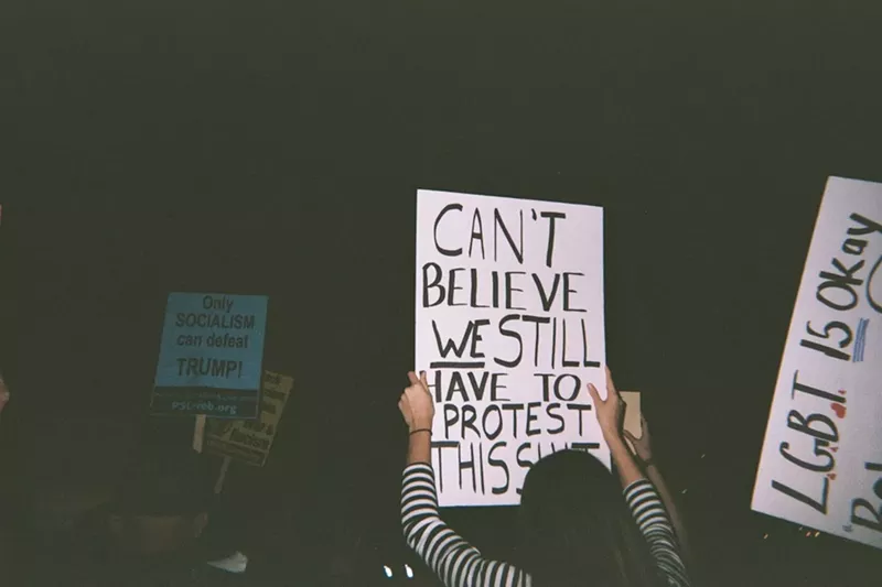 Image: Someone holds a sign that reads, "CAN'T BELIEVE WE STILL HAVE TO PROTEST THIS SHIT."