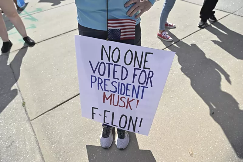Image: Someone holds a sign that reads, "No one voted for President Musk! F-ELON!"