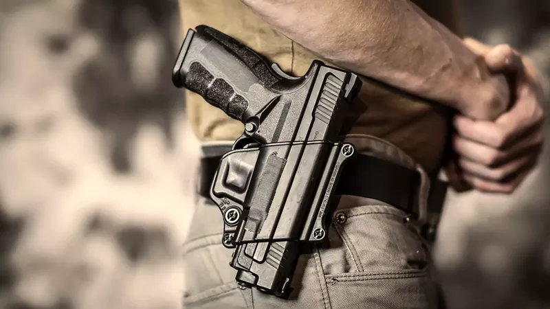 Image: close-up color photo of a holstered handgun on a man's hip