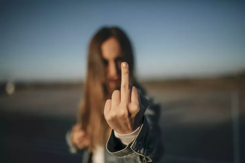 Image: Close-up of young woman outdoors giving the finger