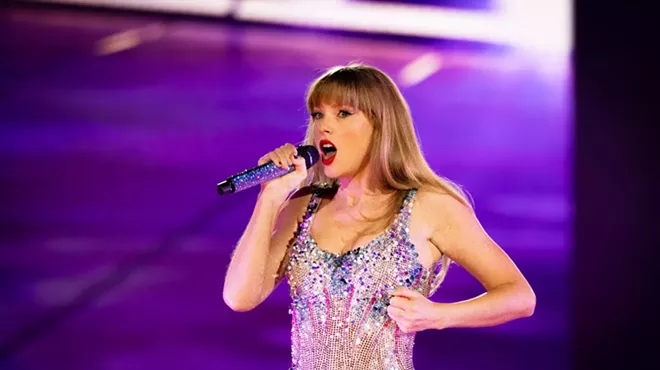 photo of be-sequined taylor swift against a purple backdrop, singing into a bedazzled wireless microphone