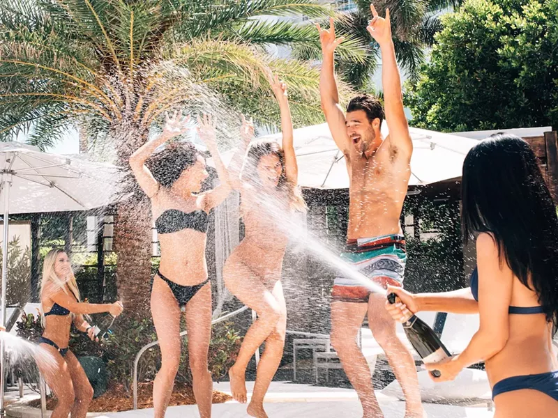 Image: three people dance as someone sprays champagne on them